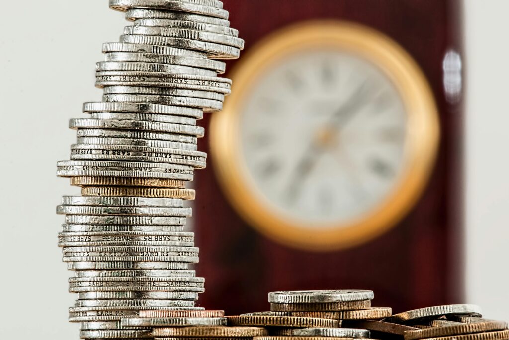 A stack of coin on a table top, with a blurry clock behind it. Treasury services by MBB Auditing.